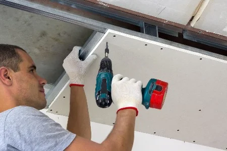 Person befestigt Trockenbauplatte mit Akkuschrauber an Decke